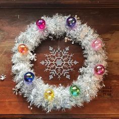 a snowflake wreath with ornaments hanging from it's sides on a wooden table