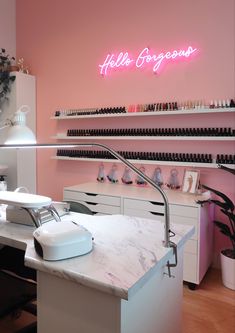 a nail salon with pink walls and white counter tops, lighted by neon lights above