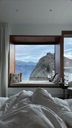 a bed with white sheets and pillows in front of a large window overlooking the mountains