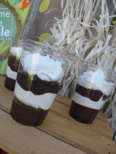 three glasses filled with dessert sitting on top of a wooden table next to a sign