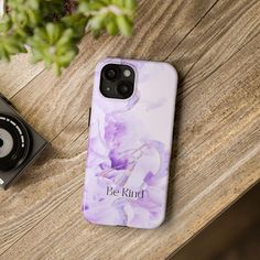 a phone case with the words be kind on it next to a camera and plant