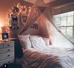 a white bed sitting in a bedroom next to a window with string lights on it