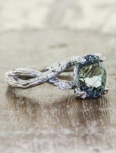 a green and white diamond ring sitting on top of a wooden table