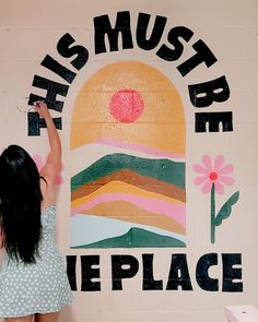 a woman painting the side of a wall with words on it that read, this must be the place