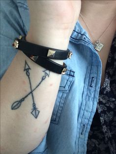 a woman with a tattoo on her arm holding onto a black leather bracelet that has an arrow and two crossed arrows