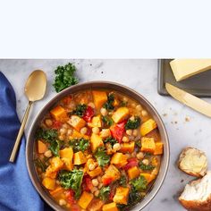 a bowl filled with vegetables and beans next to bread on top of a marble counter