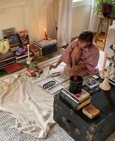 a woman is sitting on the floor in front of a table with books and candles