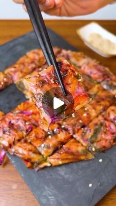 chopsticks are being used to stir food on a slate platter that is sitting on a wooden table