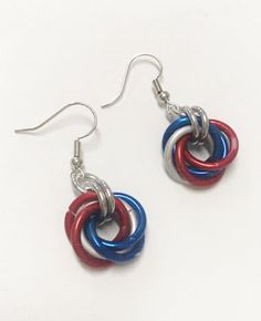 red, white and blue earrings are hanging from hooks on a white surface with silver earwires