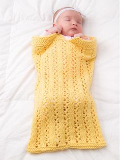 a baby wrapped up in a yellow crochet blanket on top of a bed