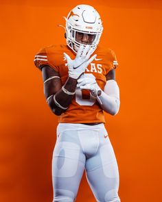 a football player wearing an orange and white uniform with his hands on his hips, standing in front of an orange background