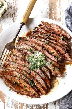 sliced steak on a white plate with parsley and garlic garnished in sauce