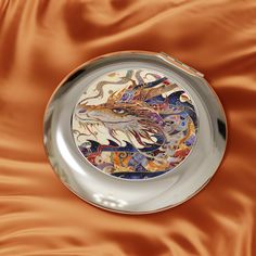 a decorative plate is sitting on an orange satin surface with the image of a dragon painted on it