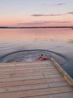 a person is swimming in the water near a wooden dock at sunset or dawn on a lake