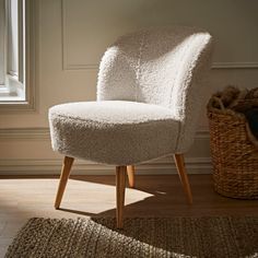 a white chair sitting on top of a wooden floor next to a basket and window