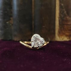 a heart - shaped diamond ring sits on a velvet surface in front of an old book