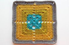 a crocheted square with a blue and yellow design on the center is sitting on a white surface