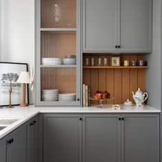 a kitchen with gray cabinets and white counter tops, along with dishes on the shelves