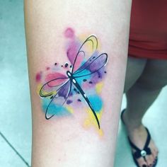 a colorful dragonfly tattoo on the left thigh and right leg with watercolor splashs