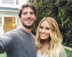 a man and woman taking a selfie in front of a house with bushes behind them