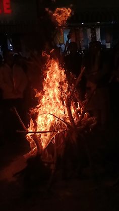 a large fire pit is lit up at night with people standing around and looking on