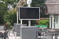 an outdoor dining area with tables, chairs and a large screen on the wall above it