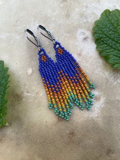 two pairs of beaded earrings sitting on top of a table next to green leaves