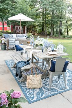 an outdoor patio with blue and white furniture, flowers on the rug, and a picnic table