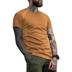 a man with tattoos standing in front of a white background wearing an orange shirt and khaki pants