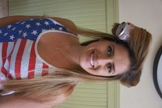 a beautiful young woman standing next to a wall with an american flag on it's shirt