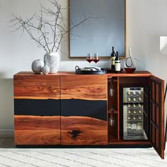 a wooden cabinet with wine glasses and bottles in it next to a mirror on the wall