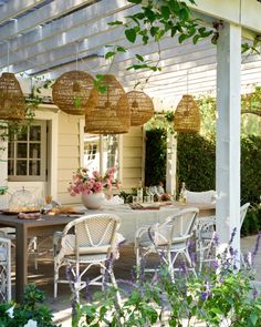 an outdoor dining area with wicker chairs and white table surrounded by greenery on the patio