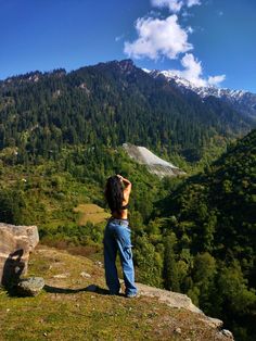 a man standing on top of a lush green hillside next to a forest covered mountain