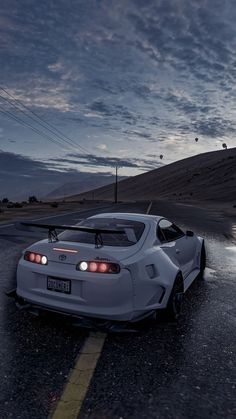 a white sports car is parked on the side of the road at night with its lights on