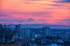 a city with tall buildings and a snow covered mountain in the background at sunset or dawn