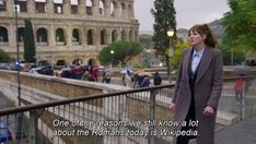 a woman standing on a bridge in front of an old building with people walking around