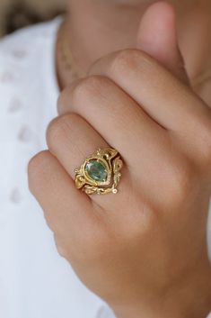 a close up of a person's hand wearing a gold ring with a green stone