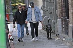 a man and woman walking their dog down the street with two other people behind them