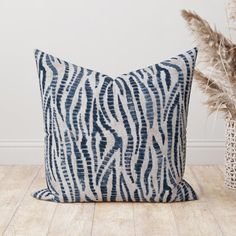 a blue and white pillow sitting on top of a wooden floor next to a plant