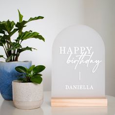 a happy birthday sign next to a potted plant on a white table with a blue vase