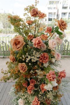 a vase filled with lots of flowers on top of a wooden table next to a fence