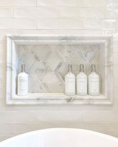 three soap dispensers in a white bathroom with marble tile and subway walls