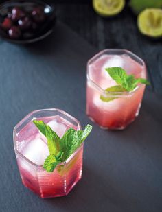 two glasses filled with fruit and ice on top of a black table next to sliced lemons