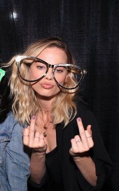 a woman wearing glasses and making the peace sign with her fingers in front of her face