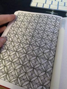 a person holding a pen and drawing something on a paper with an intricate design in it