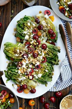 a white plate topped with lettuce and cranberries next to bowls of cherries