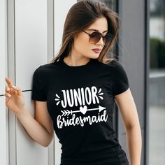 a woman wearing a black junior bridesmaid t - shirt standing against a wall