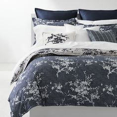 a bed with blue and white comforters, pillows and blankets on top of it