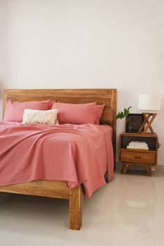 a bed with pink sheets and pillows in a white room next to a night stand