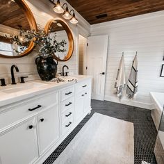 a white bathroom with black and white tile flooring, two round mirrors above the sinks